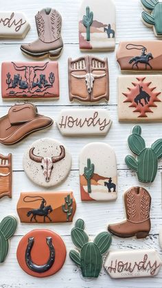 many decorated cookies are arranged on a white wooden surface, including cowboy hats and boots