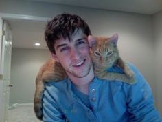 a man holding a cat on his shoulders in an empty room with carpeted floors