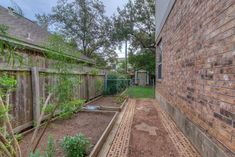 an empty garden in front of a brick building with a fence and green plants on the side