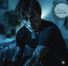 a man with tattoos sitting on a bed looking at his cell phone in the dark