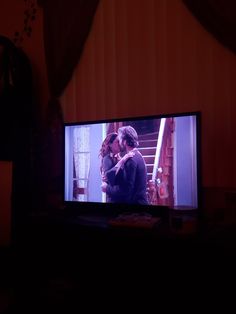 a couple kissing in front of a tv screen with the dark room behind them and curtains