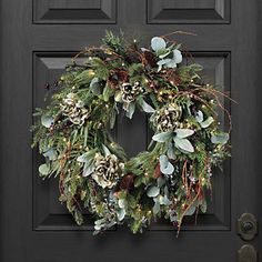 a wreath on the front door of a house decorated with greenery and pine cones