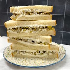 a stack of four sandwiches sitting on top of a blue and white plate in front of a tiled wall