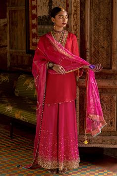 Red silk short kurta with intricate coins and floral hand embroidery on neck and sleeves . Paired with magenta hand embroidered silk sharara and dupatta with gotta finish.
Component: 3
Pattern: Embellished
Type Of Work: Gota Patti,Sequins,Coins
Neckline: V Neck
Sleeve Type: Bell Sleeves
Fabric: Silk, Organza
Color: Red
Other Details: 
Gota patti floral work sleeves
Tassel laced dupatta
Note: Outfit worn by the other model is not for sale
Occasion: Mehendi and Haldi - Aza Fashions Sharara Suit Designs, Mehendi Outfit, Kurta Sharara Set, Kurta Sharara, Indian Designer Suits, Latest Dress Design, Desi Clothes, Ethnic Outfits, Party Wear Indian Dresses