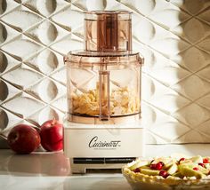 a food processor sitting on top of a counter next to an apple pie and some apples