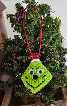 a green ornament hanging from a christmas tree with eyes and nose on it