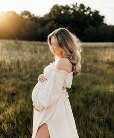 a pregnant woman in a white dress is standing in the grass with her legs crossed