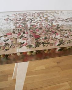 a glass table with flowers on it and a white ribbon tied around the edge, in front of a wall