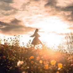 a woman is walking through a field full of wildflowers and the sun shines brightly in the background