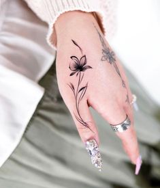 a woman's hand with a flower tattoo on her left thumb and ring finger