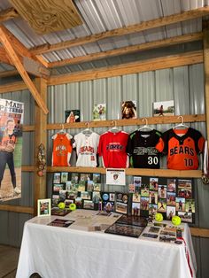 a table with baseball jerseys on display in a room next to a metal wall and wooden beams