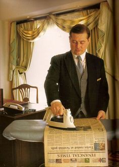 a man in a suit ironing a newspaper with an iron on the table next to him