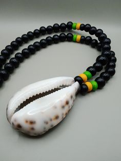 The large halved Cowrie shell is approximately 2 inches wide and 2.50 inches long. The necklace is beaded with wooden beads. The beads are green, yellow and black. The beads are 10 to 12 mm. If you have any questions please feel free to contact us at anytime. All shipping options are available. All items will be shipped out Monday through Friday. Receipts will be emailed out for immediate access. All items will be shipped out carefully and every shipment can be made with extra insurance upon req Black Necklaces With Large Beads For Beach, Black Wooden Beads For Beach, Black Wooden Beads Necklace For Beach, Handmade Black Shell Necklaces, Cowrie Shell Necklace, Shell Necklace, Cowrie Shell, Yellow And Black, Black Gift