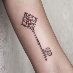 a small key tattoo on the arm with a red stone embedded in it's center