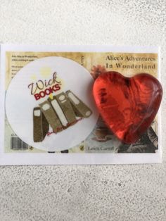 a red heart sitting next to a piece of paper on top of a white surface