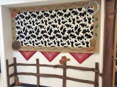 a cow themed wall hanging on the side of a building with a wooden fence in front of it