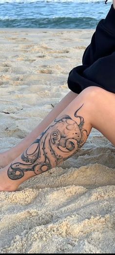 a woman sitting on the beach with her legs crossed and an octopus tattoo on her leg