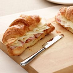 a croissant sandwich cut in half on a cutting board with a knife and fork