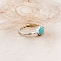 a gold ring with a turquoise stone in the middle on top of a piece of wood