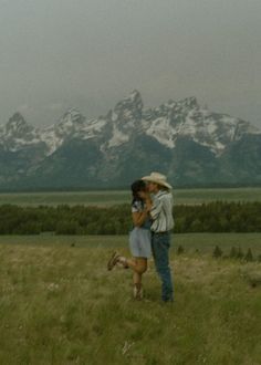 a man and woman kissing in front of mountains