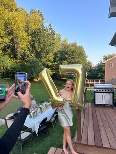 a woman holding up a letter balloon in front of a man taking a photo with his cell phone