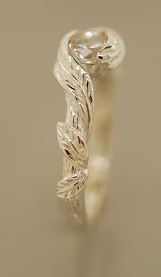 a white gold ring with leaves on the sides and a diamond in the center, sitting on a table