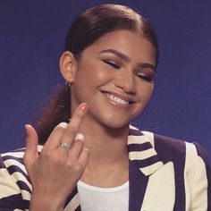 a young woman smiles as she holds her hand up to the side with one finger