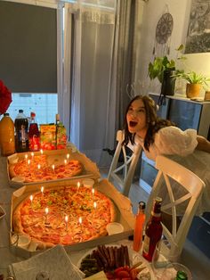 a woman sitting at a table with three pizzas in front of her and candles on them