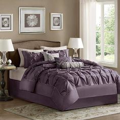 a bed with purple comforter and pillows in a bedroom next to two lamps on a table