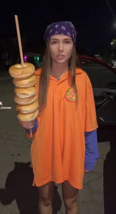 a woman holding a stack of doughnuts in her hand and wearing an orange shirt