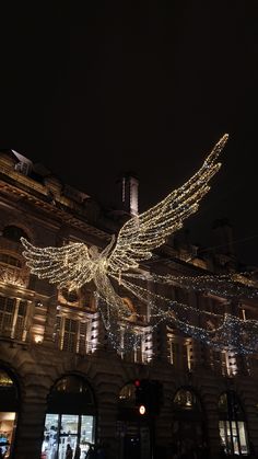 an angel statue is lit up in front of a building at night with lights on it