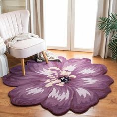 a large purple flower rug in a living room next to a white chair and potted plant