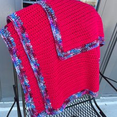 a red crocheted blanket sitting on top of a metal chair next to a door