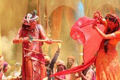 two people dressed in red and orange dancing with colored powder