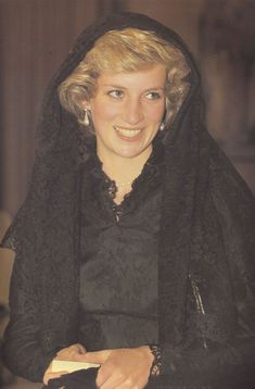 a woman wearing a black shawl and holding a book in her right hand while smiling at the camera