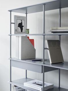 a book shelf with several books and magazines on it in a white walled room next to a wall