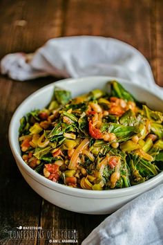 a white bowl filled with cooked vegetables on top of a wooden table next to a napkin