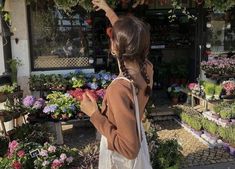 a woman is pointing to the sky in front of a flower shop with lots of potted plants