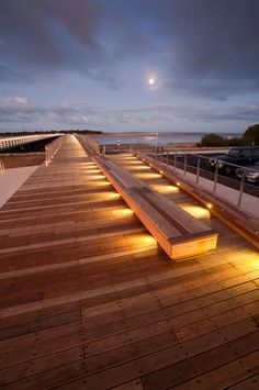 a long bench sitting on top of a wooden deck next to the ocean at night