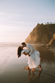 a couple kissing on the beach in front of an ocean and cliff at sunset or sunrise