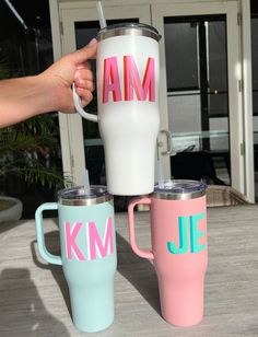 three different colored coffee mugs sitting on top of a wooden table next to each other