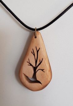 a wooden pendant with a tree on it hanging from a black leather necklace cord against a white wall