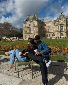 a man and woman sitting on a bench in front of a large building with flowers