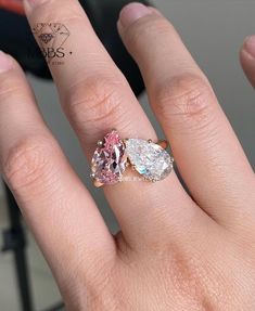 a woman's hand with two engagement rings on top of her finger, and the other side has an oval shaped pink diamond