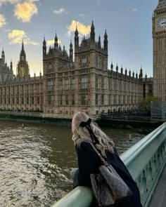 a woman standing on the edge of a bridge looking at big ben in london, england