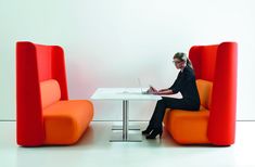 a woman sitting at a table with a laptop in front of her on an orange chair