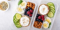 two plastic containers filled with food on top of a white table next to bowls of fruit and nuts