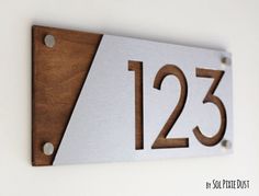 a house number sign mounted to the side of a wall with wood and metal numbers on it