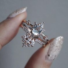 a woman's hand holding an engagement ring with diamonds on it and a white manicure