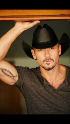 a man wearing a black cowboy hat and holding his arm behind his head with one hand